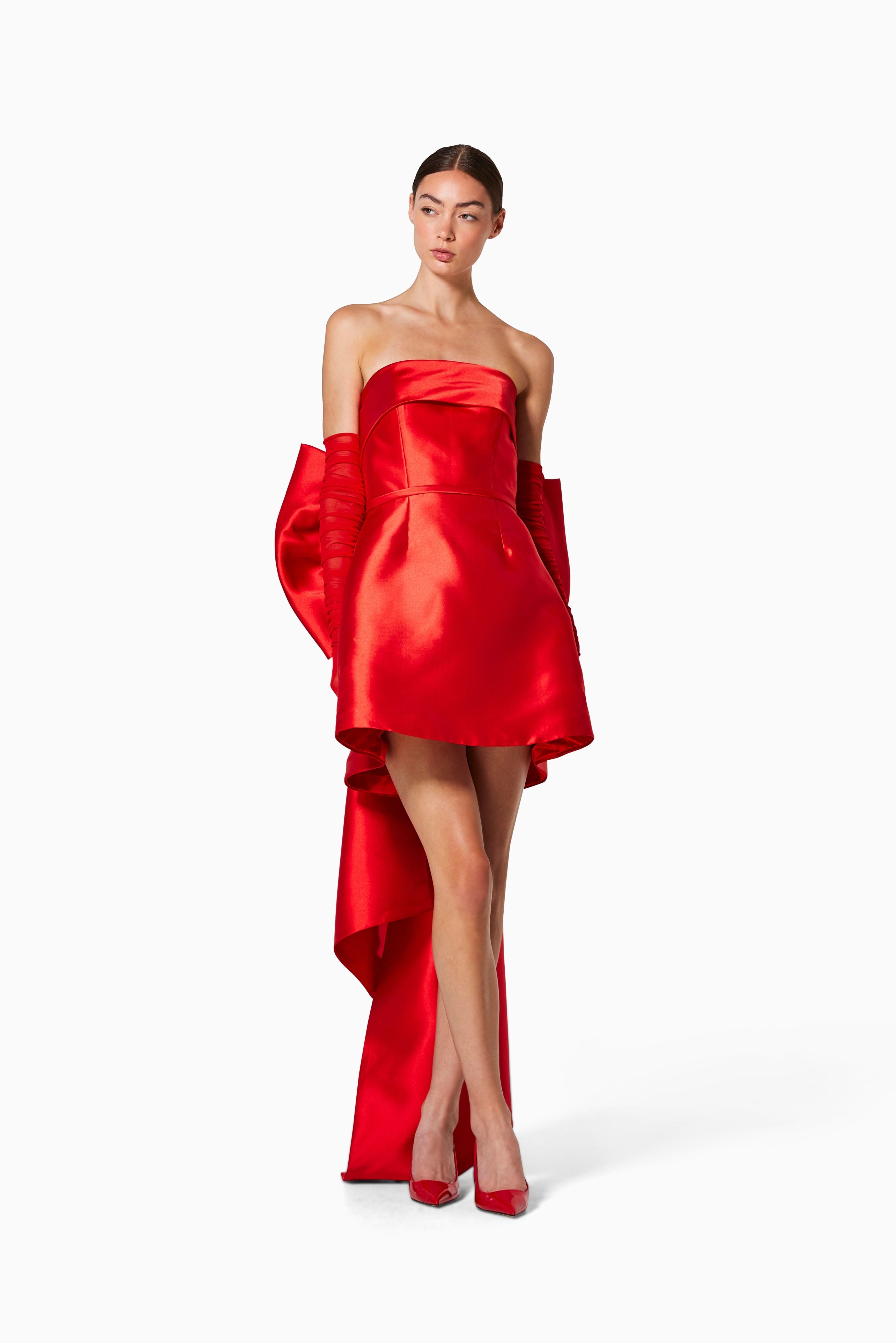 Woman wearing a red strapless dress with a high-low hem on a white background