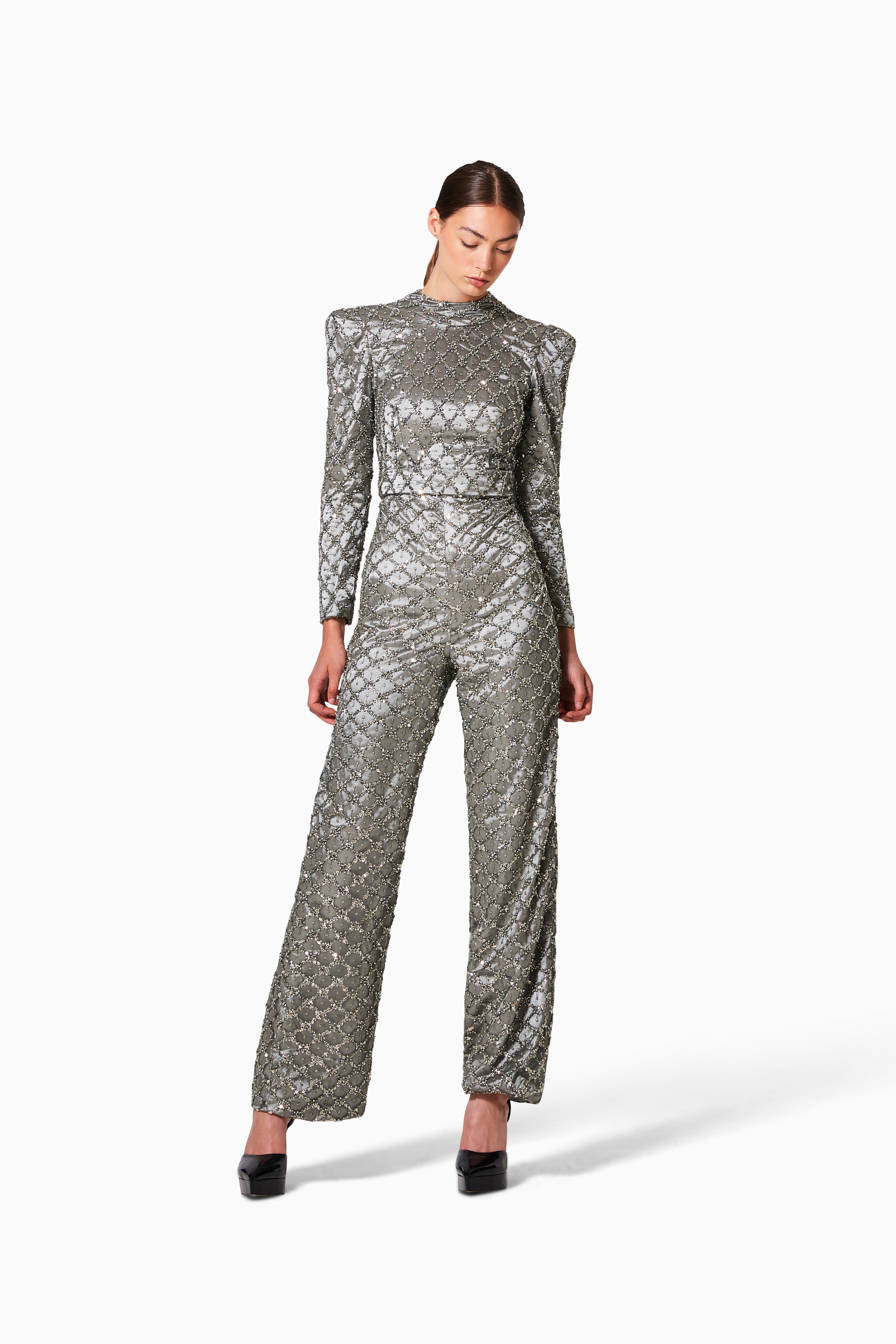 A model wearing a gray beaded embroidered one-piece suit with strong shoulders and a high neck.
