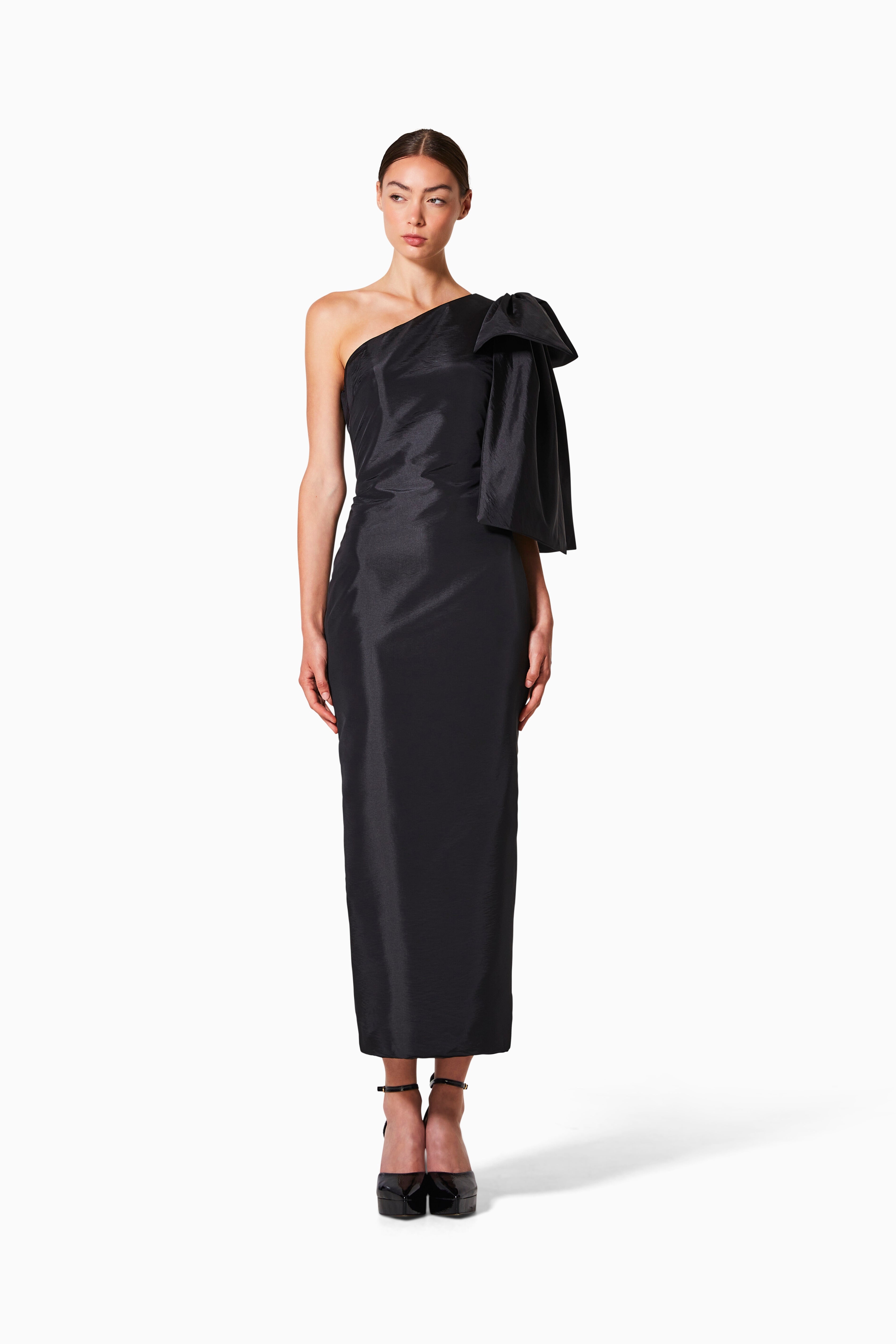 A model wearing a black silk taffeta bias-cut dress with a bow detail, standing against a white background.