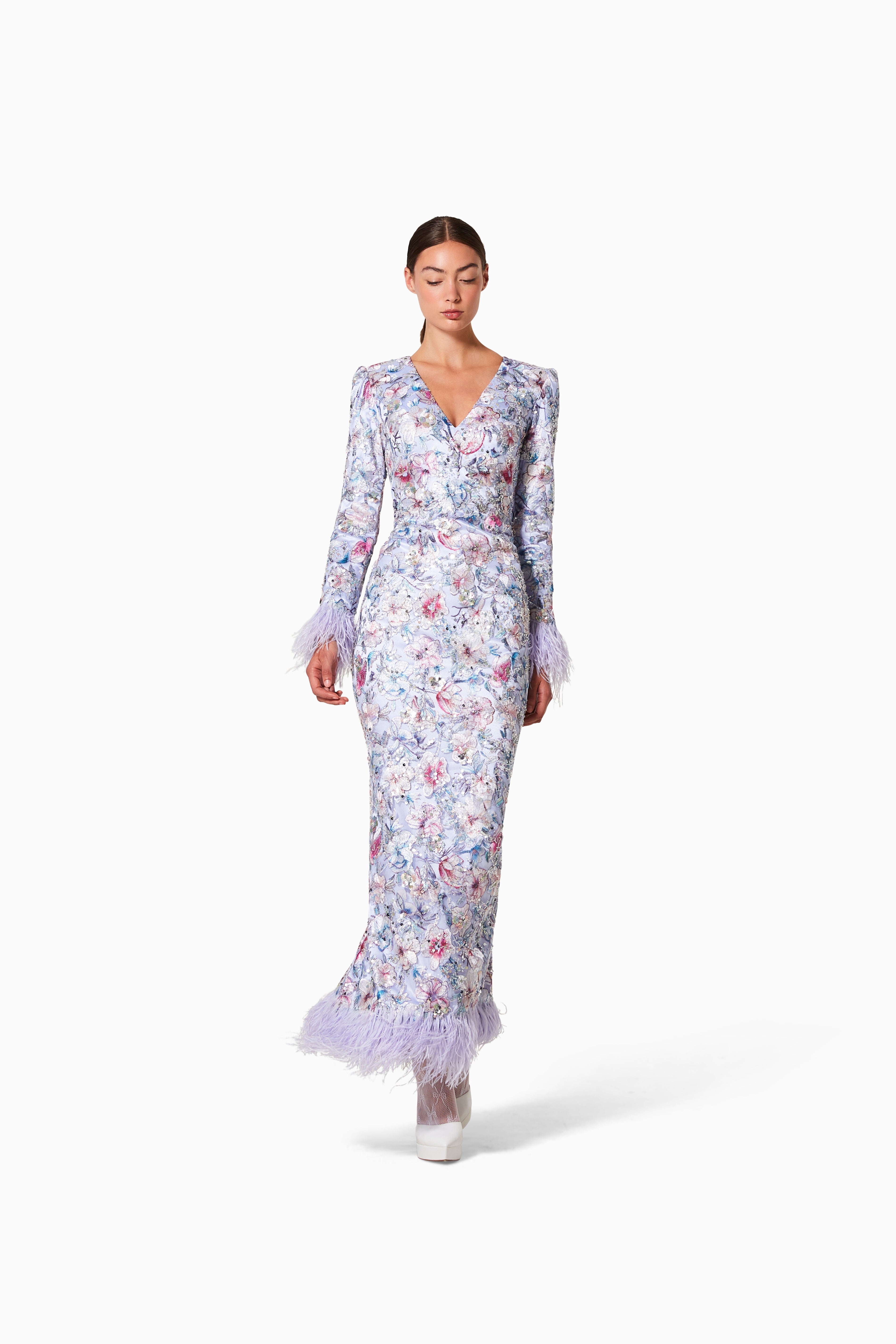 A woman standing and modeling a floral kimono dress with embroidery and feathers.