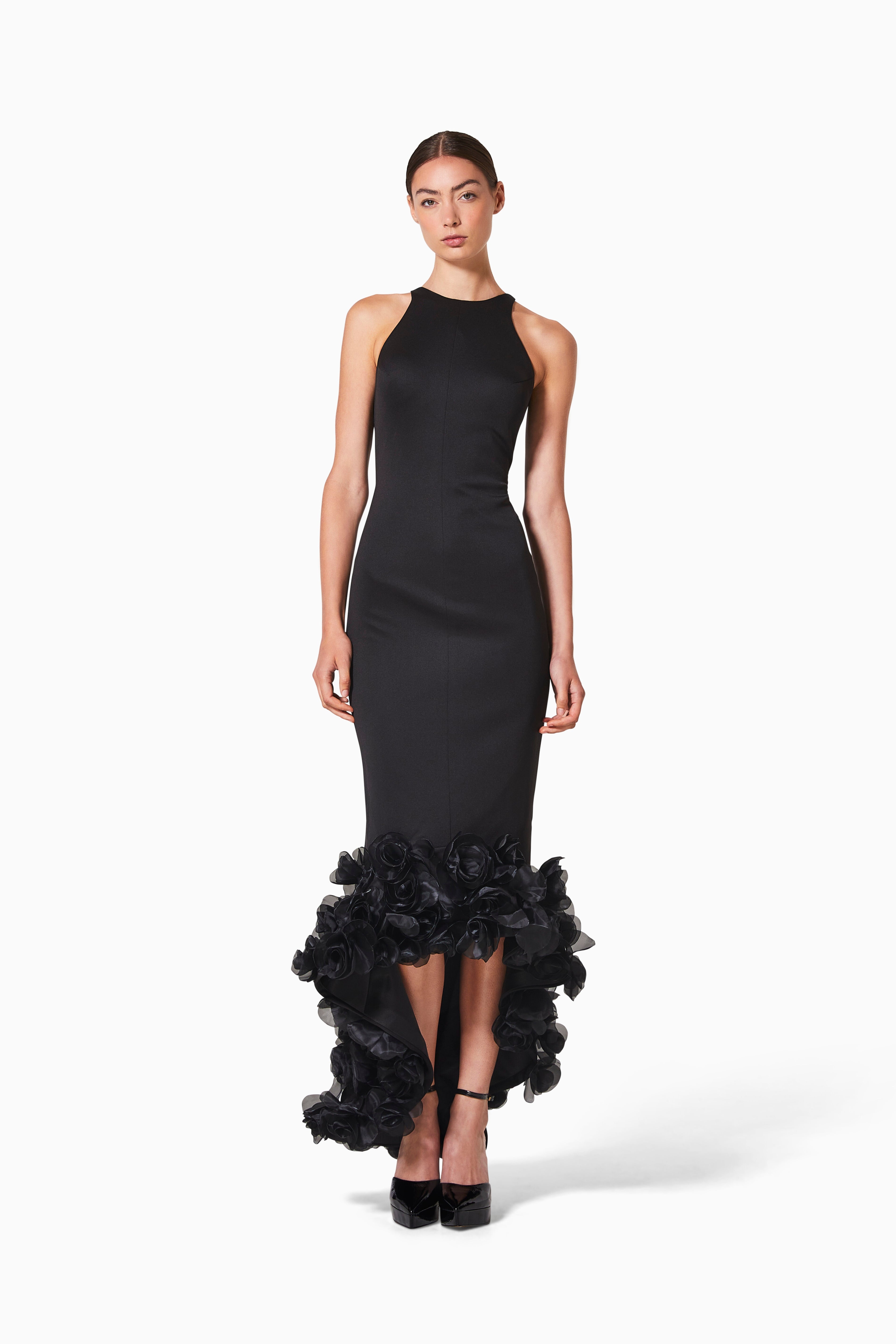 A woman modeling a chic black dress with rosette details trimming the hem, made from tencel fabric.