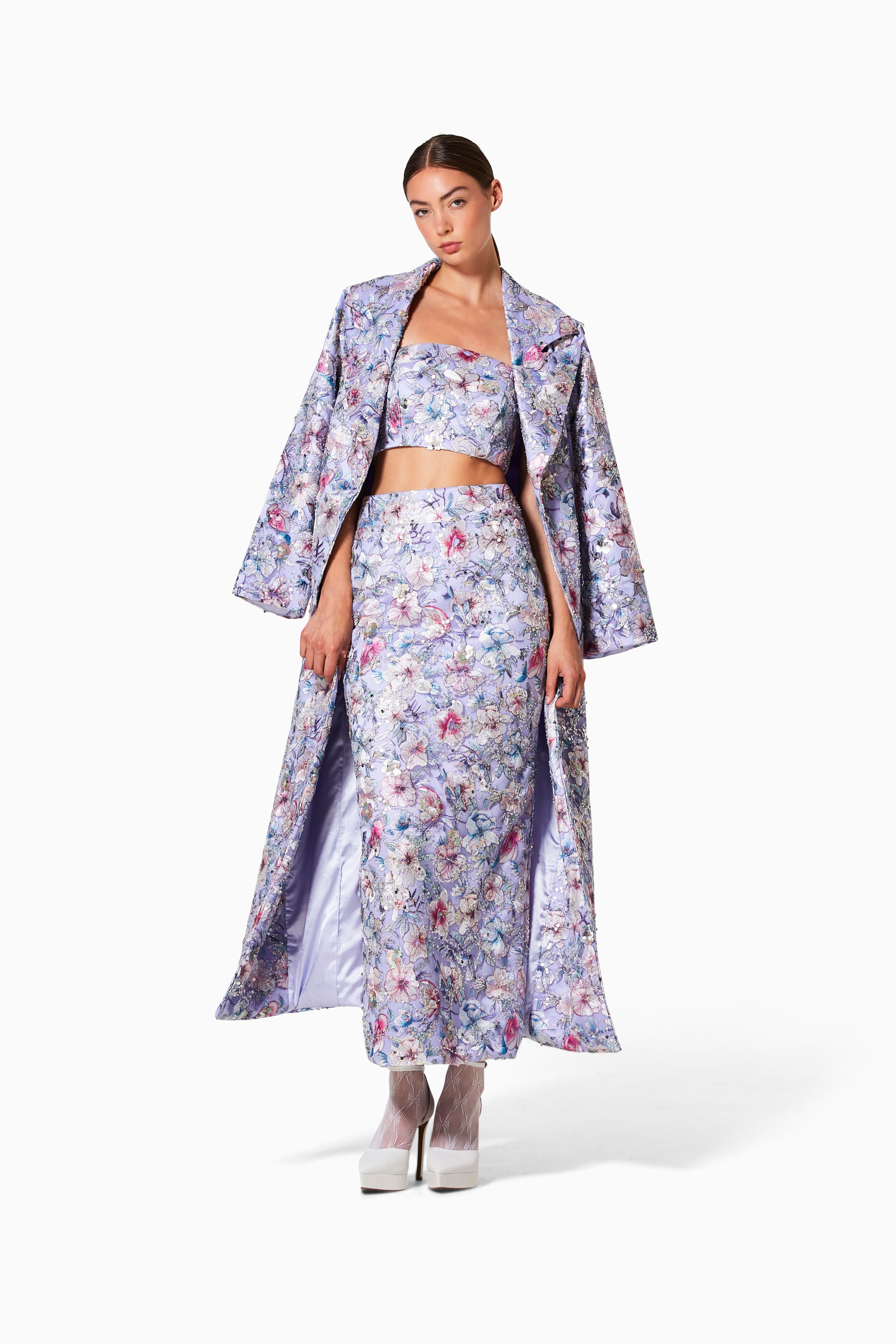 A female model wearing a floral embroidered coat with satin lining and a matching skirt, standing against a white background.