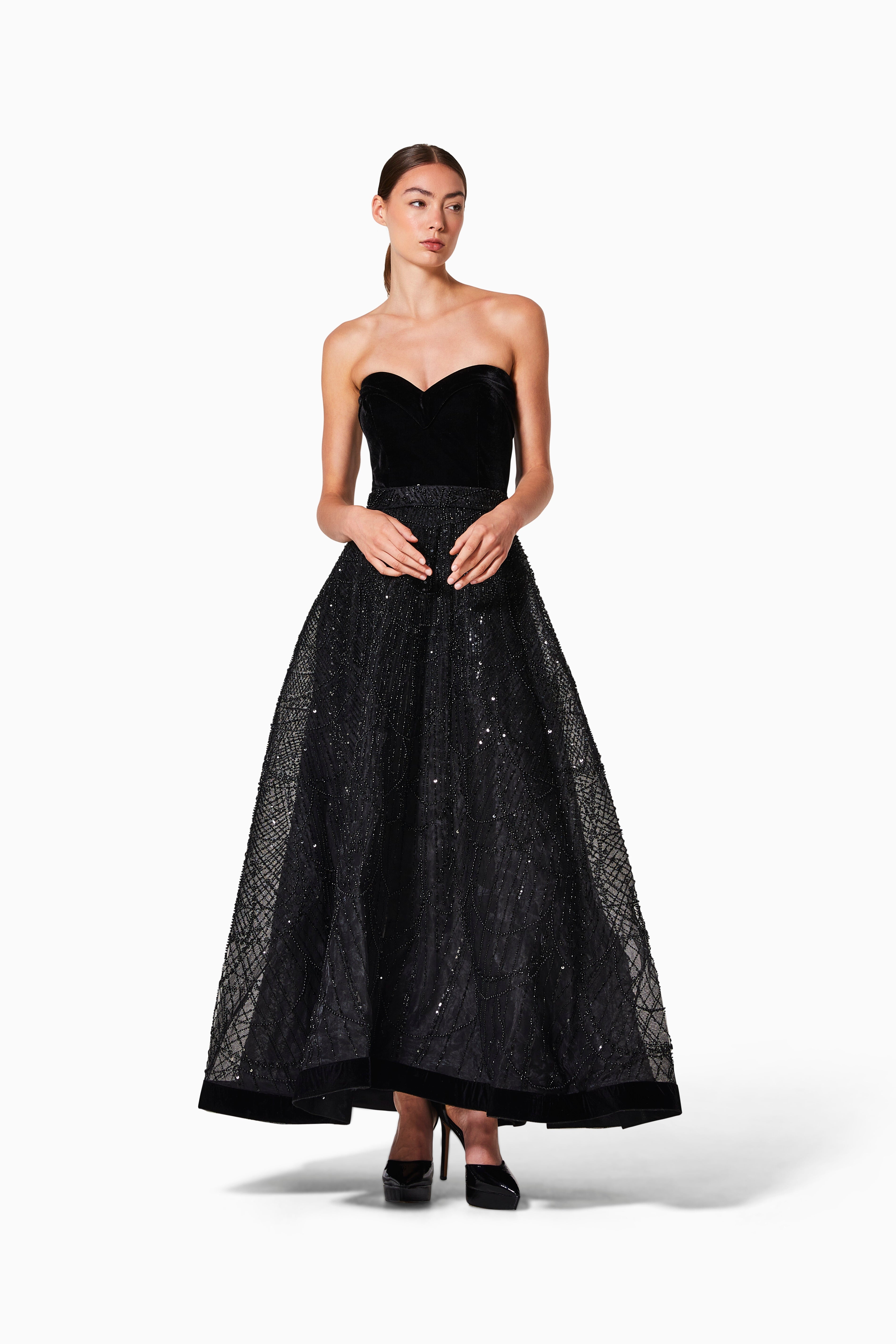 A woman modeling a black velvet cocktail dress with a strapless top and sequin embroidery on the skirt.