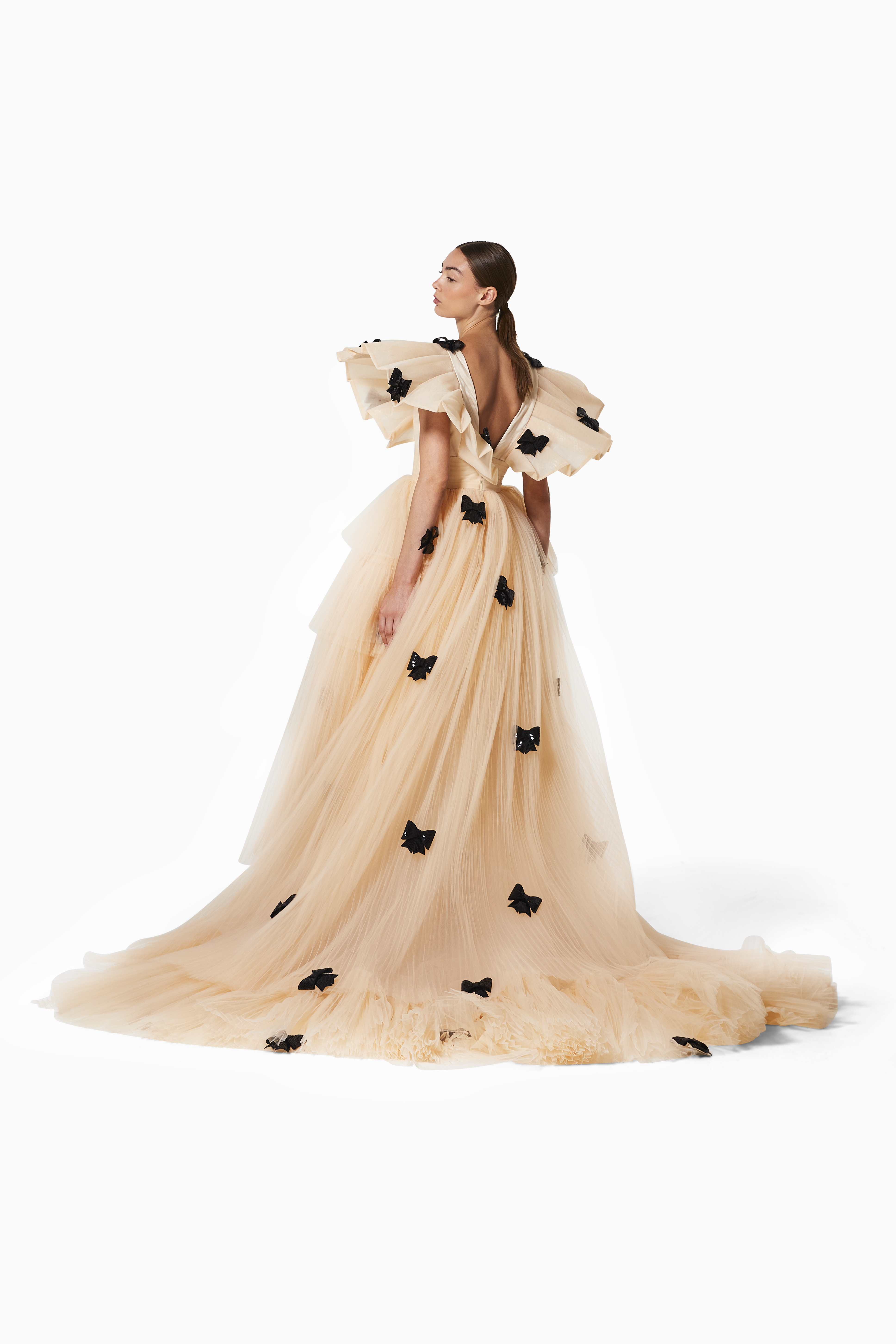 Woman wearing a beige evening gown with black floral details on a white background