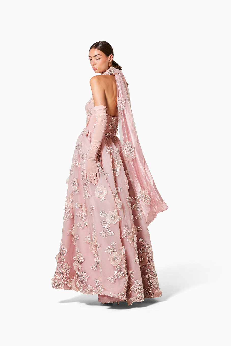 Woman wearing a pink embroidered gown with a sheer overlay on a white background