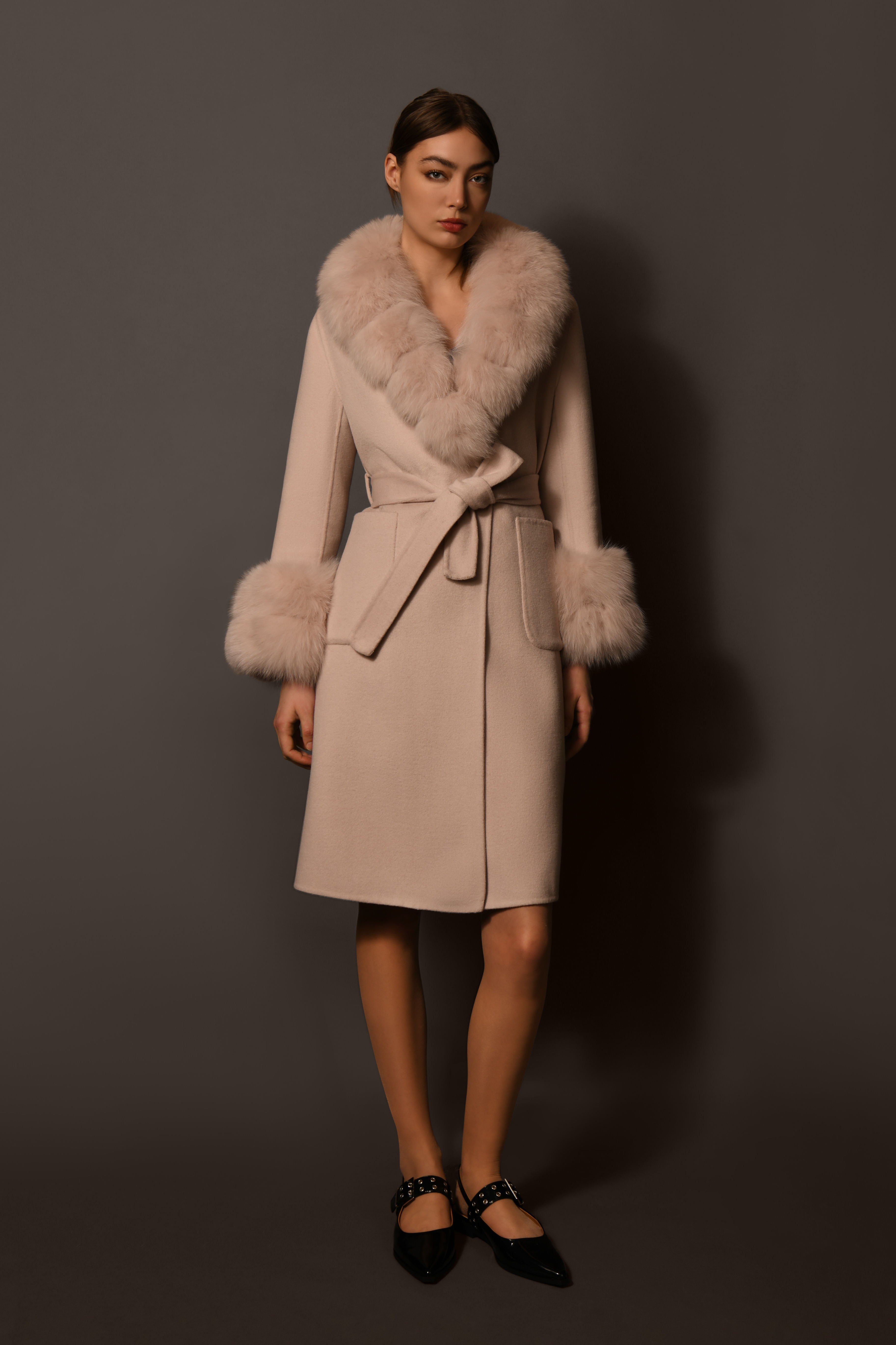 Woman wearing a beige coat with fur trim against a dark background