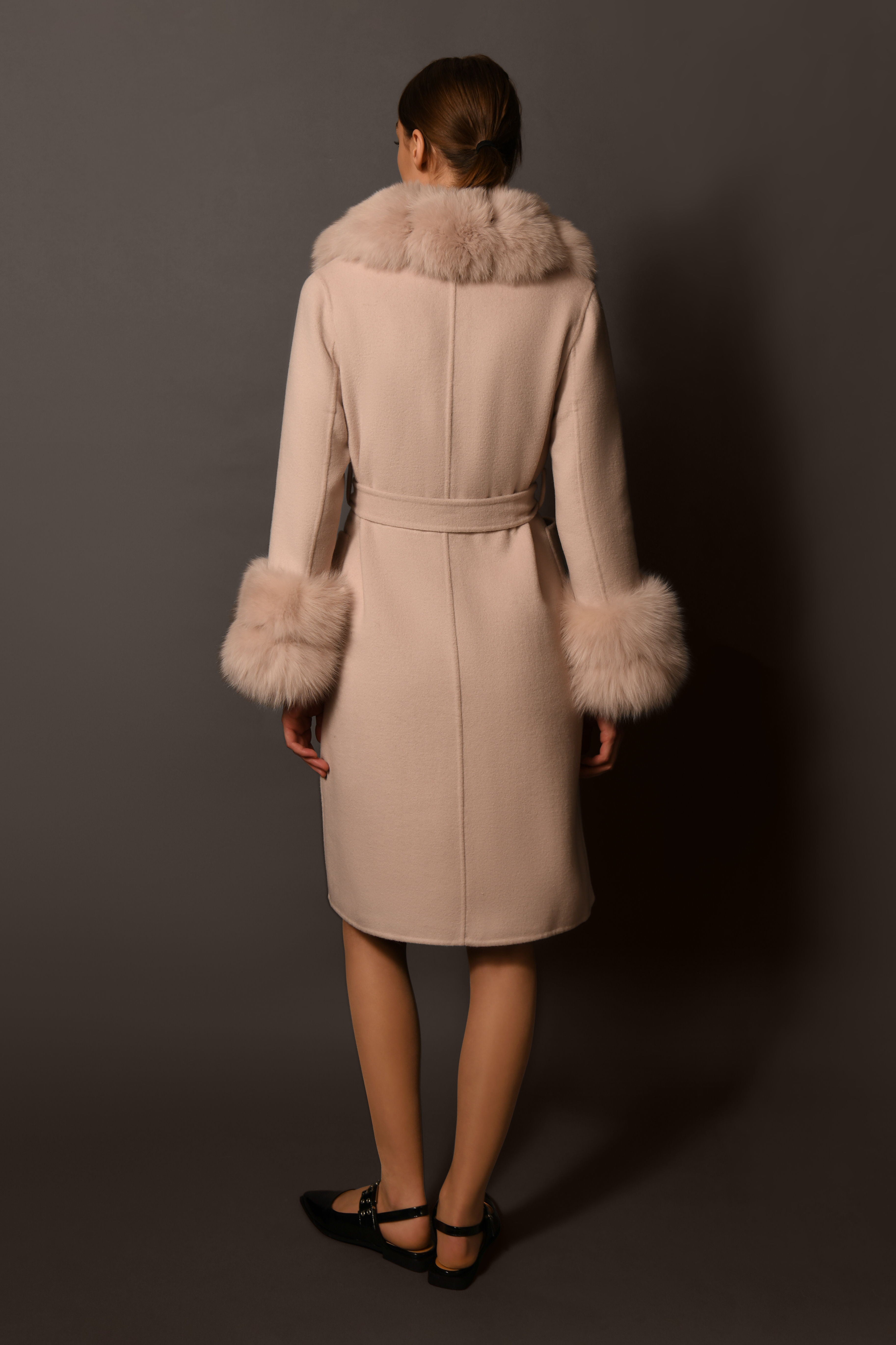 Beige coat with fur trim worn by a person on a gray background